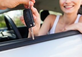 young smiling woman sitting in car taking key handover rent  purchase